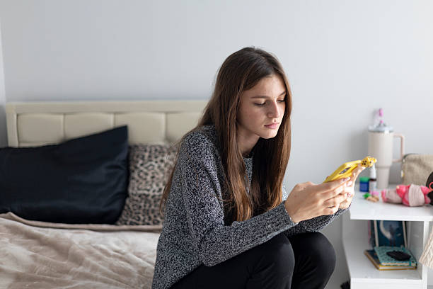 istock Young woman sitting on a bed, focused intently on her smartphone screen 2244574888