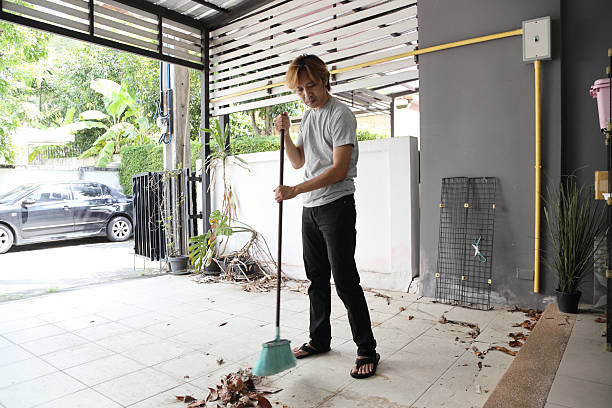 The Southeast Asian man is cleaning and sweeping the leaves in front of the house.