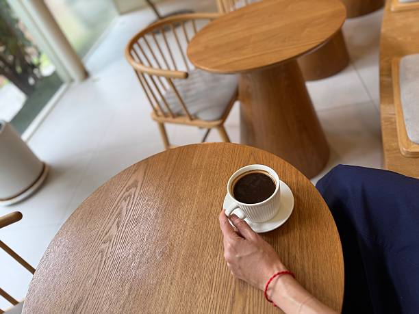 A woman’s hand holding a cup of coffee on a wooden table — top view, copy space