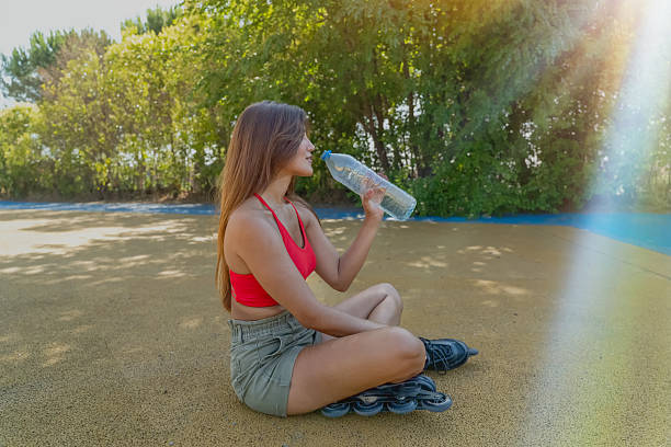 istock Woman sitting on ground in park drinking water from bottle, taking a break from roller skating 2244581743
