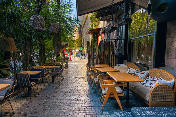 Yerevan, Armenia 10.16.2025. A sidewalk with tables and chairs outside of a restaurant. The tables are covered with white cloths and the chairs are wooden. The chairs are arranged in a way that they face the street