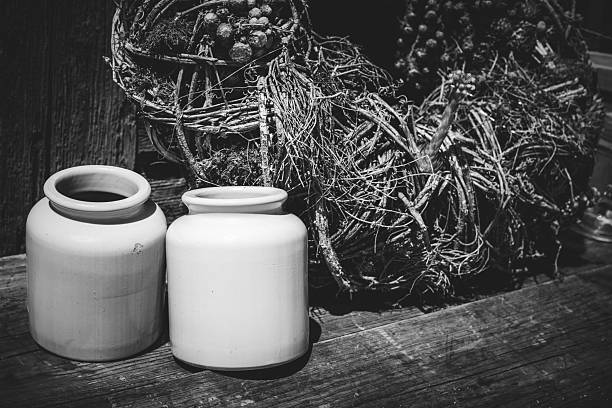 Monochrome photograph of two matte ceramic jars with a rustic twig wreath on a wooden surface.