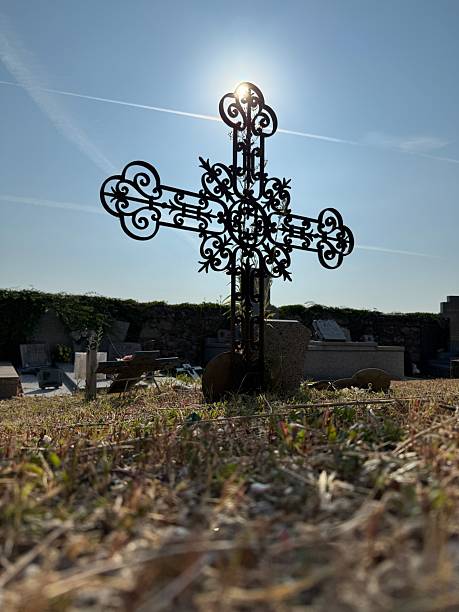 Sunlight shining through ornate iron cross in a peaceful cemetery