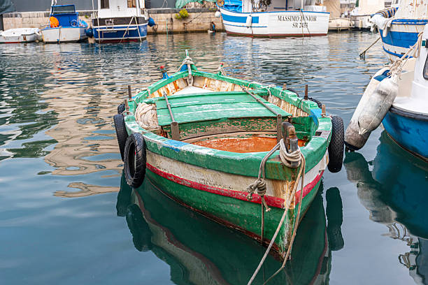 Syracuse, Sicily, Italy - October 20, 2025: Fishing boats moor at a charming harbor in Syracuse, Sicily, Italy, calm waters, and urban surroundings. Capturing a vibrant coastal Italian scene with traditional boats and docks.