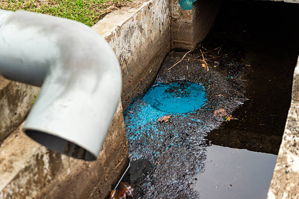 istock Drainage pipe discharges bright blue liquid into murky water within a concrete structure. 2244610163
