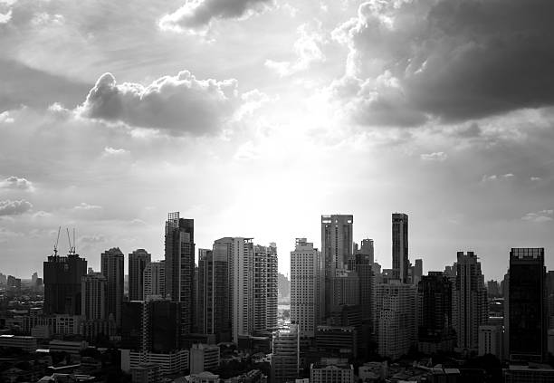 Dramatic Black and White Cityscape with Modern Skyscrapers and Clouds against Bright Sun Flare  Urban Skyline View