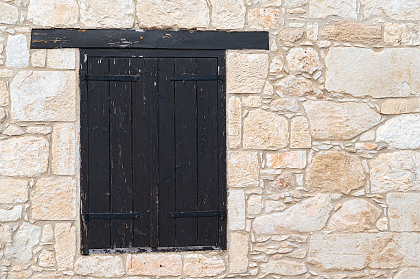 Rustic black wooden shutters elegantly set against a textured stone wall, perfectly showcasing their aged charm