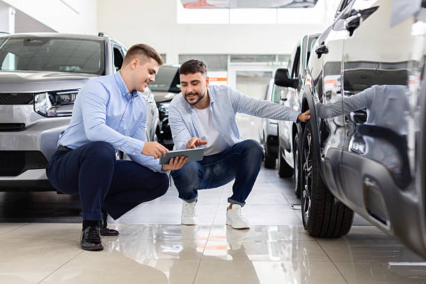 istock Smiling salesman and customer crouching near car, discussing details using tablet 2244617139