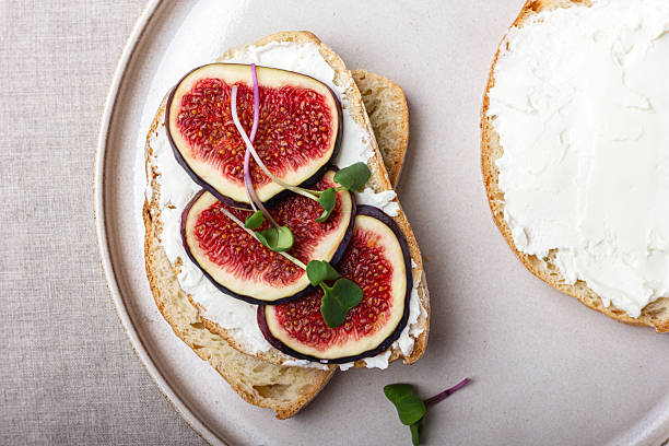 Bread with young cream cheese, freshly sliced figs and radish sprouts. A delicious appetizer for wine on the table with a beige tablecloth.