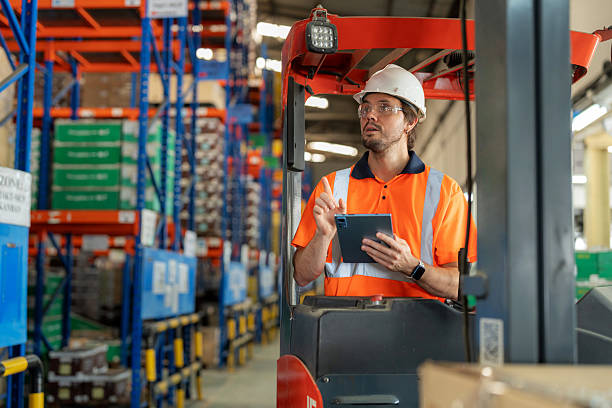 istock A warehouse employee in reflective safety clothing checks a digital tablet while operating a forklift to arrange goods on racks. Smart logistics, supply chain efficiency, and intelligent transportation technology in modern industry. 2244621164