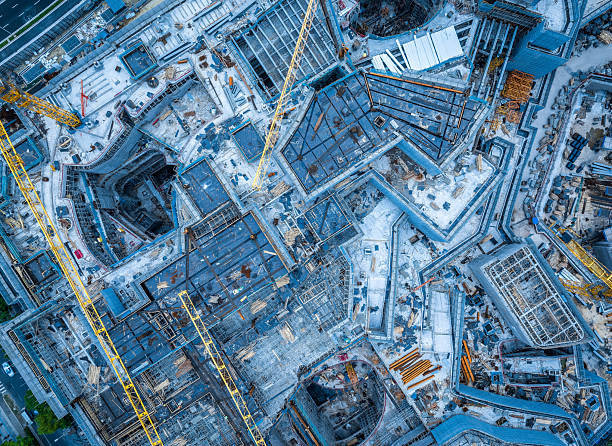 Top down view of a large modern building construction site with heavy machinery and complex steel structures.