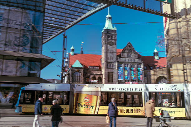 Chemnitz, Germany - March, 7, 2025: A city tram passing by the main tram station while people are crossing the street towards the St. Jacobs church and the shopping mall.  Motion blur.