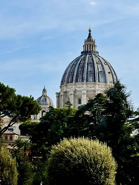 A bright day view of Saint Peter's Basilica, showcasing its striking dome and statues under a vivid blue sky. The architecture signifies historical and religious importance in Vatican City.