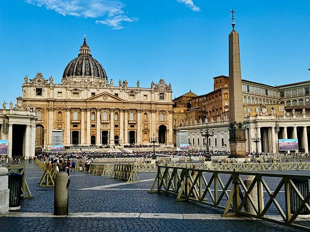 St. Peter’s Basilica, crowned by its majestic dome, dominates the skyline above St. Peter’s Square. Below, the central obelisk stands amid sweeping colonnades as crowds of visitors gather under a bright, open sky—capturing the heart of Vatican City and centuries of spiritual and architectural grandeur.