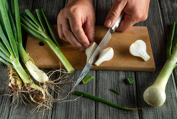 istock Hands skillfully slice green onions on a wooden board, surrounded by fresh vegetables. The scene captures a moment of food preparation in a cozy kitchen 2244640222