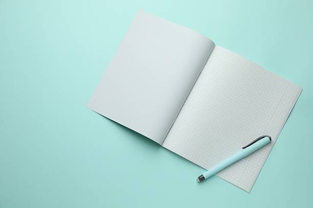 Open copybook with checkered sheets of paper and pen on light blue background, top view. School stationery