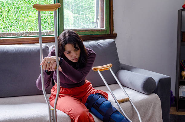 istock Sad young woman with crutches with a broken leg sitting on a couch. 2244653664