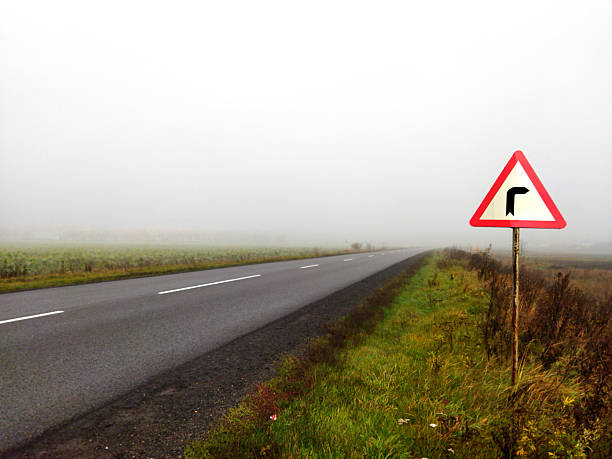 Visibility is low on a winding road surrounded by fog.
