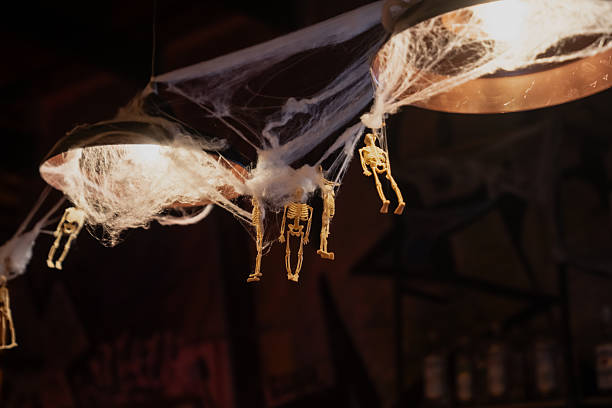 istock Halloween ceiling decoration with small hanging skeletons and artificial spider webs illuminated by warm light, detailed festive setup creating spooky interior atmosphere and seasonal design 2244657958