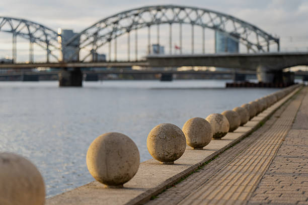 Daugava river promenade in Riga with aligned stone spheres and bridge silhouette representing urban geometry, symmetry, and architectural composition in scenic Baltic capital city environment