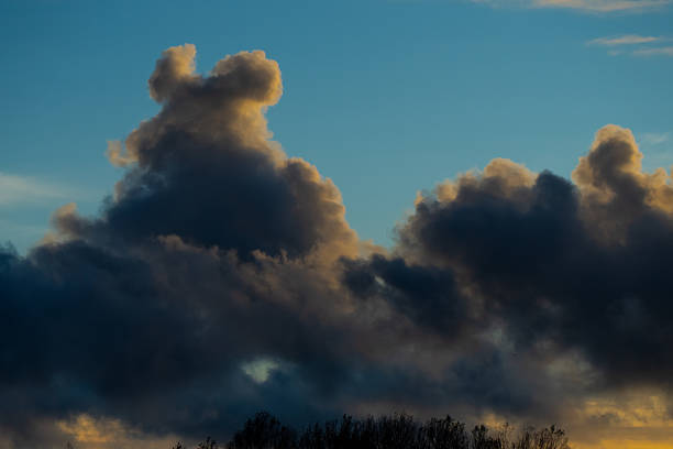Heavy clouds forming above trees in Riga during sunset showing light contrast, layered atmosphere, and dramatic evening pattern over natural autumn skyline