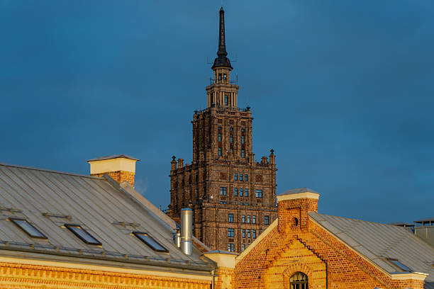 Riga Academy of Sciences tower and old brick rooftops illuminated by warm sunset light showing historical architecture contrast, urban skyline composition, and evening atmosphere