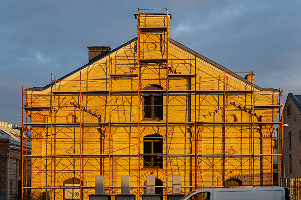 Historic brick building facade under renovation with steel scaffolding structure and arched windows showing construction stabilization process and architectural restoration in urban environment