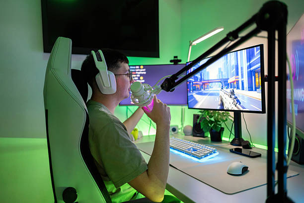 istock Young man wearing headset and talking into microphone, playing first-person shooter on computer for online community 2244662284