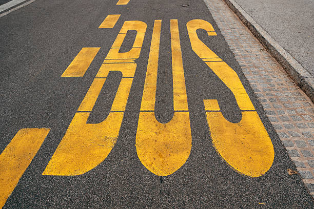 Yellow bus stop sign painted on black asphalt road surface, high angle view