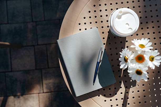 istock Notebook, pen, coffee, and flowers on a sunny outdoor table 2244666221