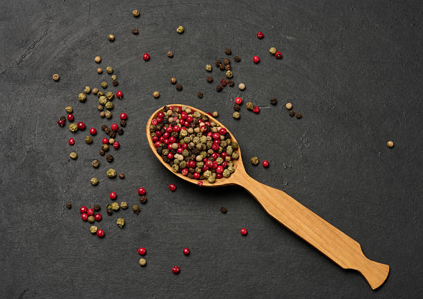 istock Mixed dry peppercorns in a wooden spoon on a black table, top view 2244669004