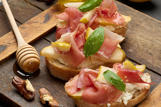 istock Delicious appetizer of bruschetta with pear, prosciutto and cheese. Dish is presented on a wooden board 2244669335