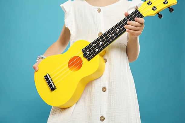 Little girl with ukulele on light blue background, closeup