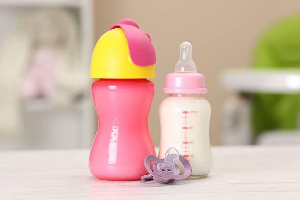 Feeding bottles with milk and pacifier on white wooden table indoors