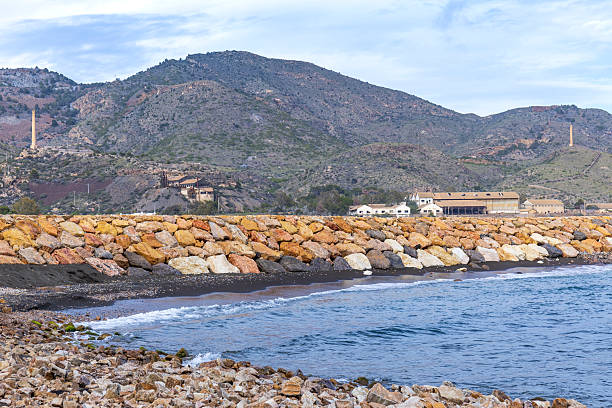 View of the coast and bay of Portmán in the jetty area, with the mining mountain of Cartagena-La Unión as a backdrop, featuring enduring mining installations.