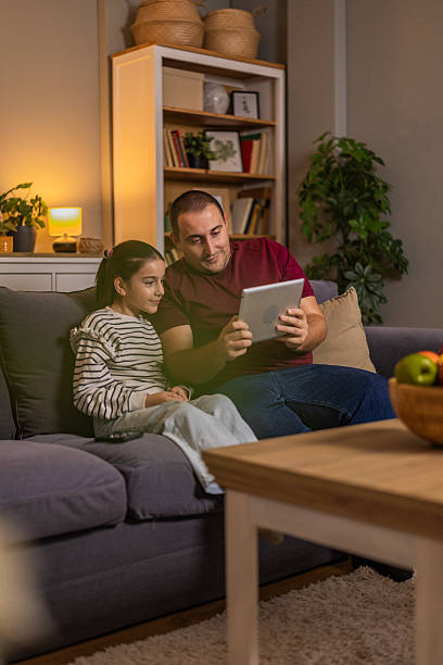 istock Dad and his daughter using tablet browsing internet together and watching movie online or making video call while sitting on the sofa in the living room. 2244679002