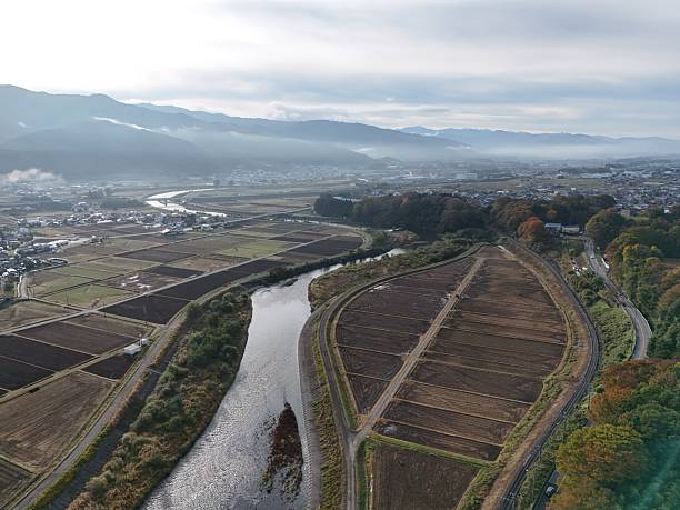 A river runs through a valley with a city in the background. The sky is cloudy and the mood of the image is peaceful and serene