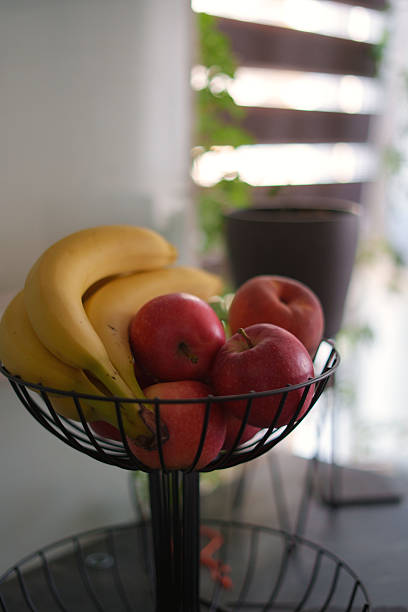 istock cozy kitchen setting featuring a wire fruit basket with fresh red apples and yellow bananas against a softly lit background with plants and blurred decor elements, peaceful, inviting, relaxed 2244682642