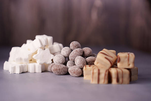 istock a tempting assortment of white star-shaped marshmallows, sugar-dusted almonds, and creamy chocolate-dipped fudge squares against a soft purple wood-grain background, decor, variety, decadent 2244682690