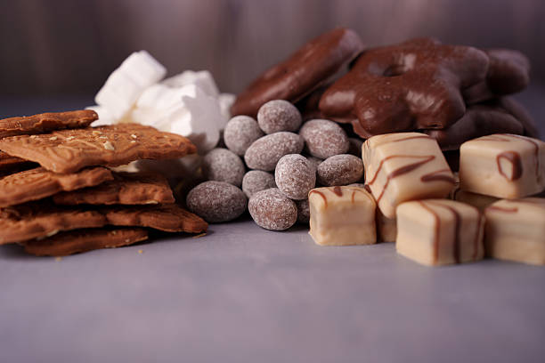 istock assortment of diverse confectionery items including biscuits, marshmallows, chocolate-covered treats, sugar-dusted nuts, and white chocolate cubes on a soft gray surface, baked, arrangement 2244682701