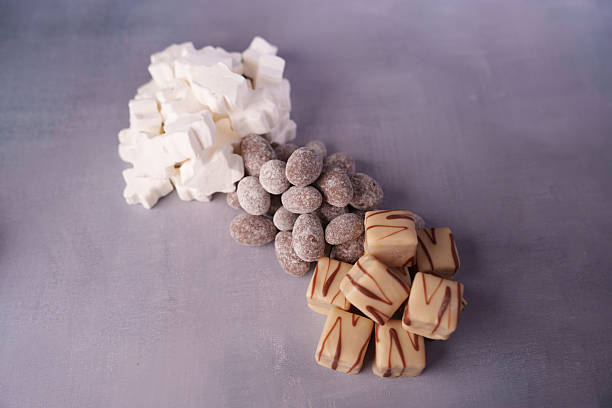 a trio of sweet treats arranged on a textured surface, featuring white marshmallows, chocolate-covered almonds, and drizzled caramel squares, creating a delightful blend of flavors and textures