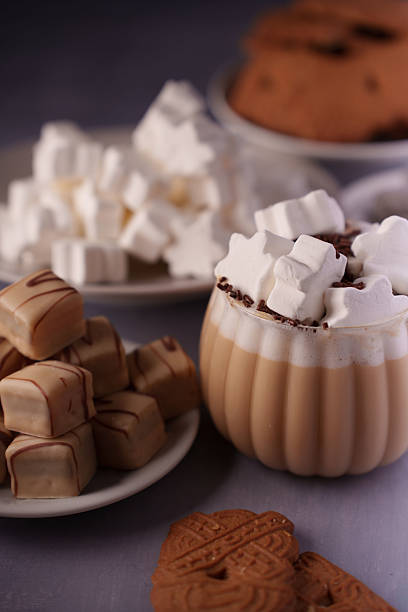 istock cozy table scene featuring a mug of frothy hot chocolate topped with marshmallows, alongside plates of bite-sized chocolate-coated caramel cubes and classic shortbread cookies, comforting, plated 2244682747