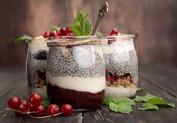 Close-up of four glass jars filled with chia pudding, yogurt, granola and fresh pomegranate seeds. Vegan healthy breakfast concept with mint decoration.