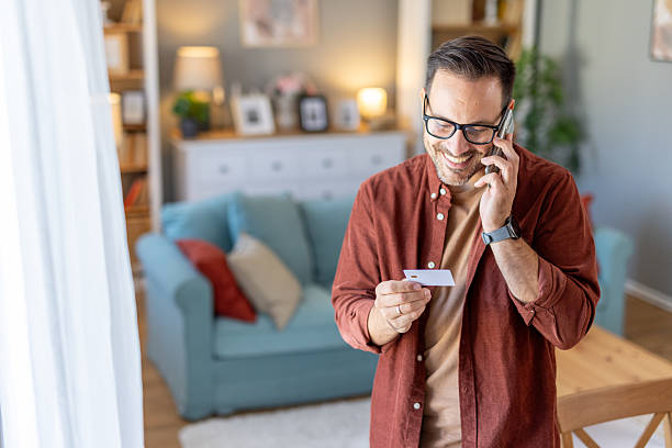 istock Man talking on phone and holding a card in a warm setting. 2244694279