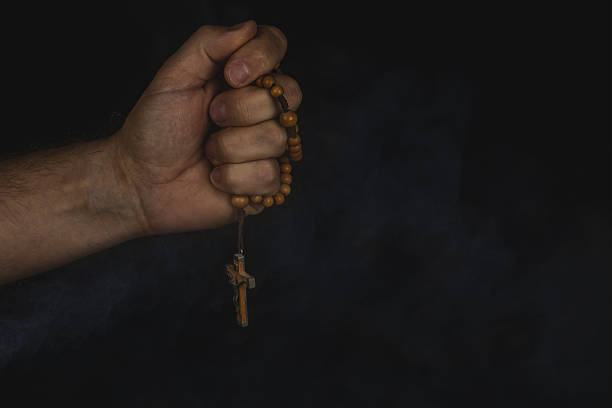 A hand firmly grips a wooden rosary with a cross, set against a dark backdrop. The gesture suggests prayer or contemplation, evoking a sense of spirituality.