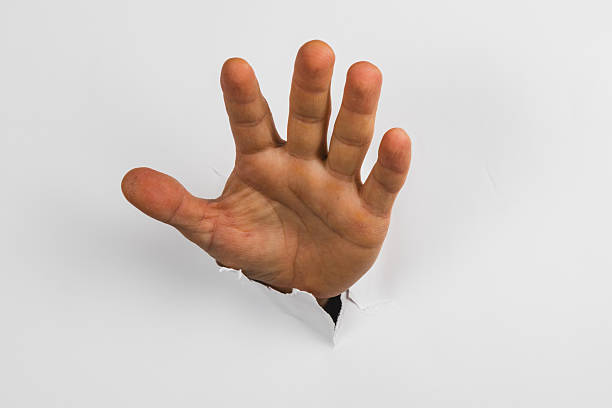 istock Hand reaching through a wall creates illusion and surprise 2244706095