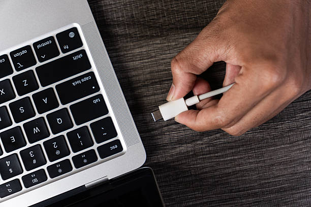 Hand Connecting a White USB C Plug to a Dark Gray Laptop Keyboard stock photo