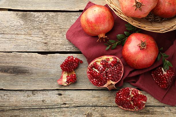 istock Fresh pomegranates and green leaves on wooden table, top view. Space for text 2244715041