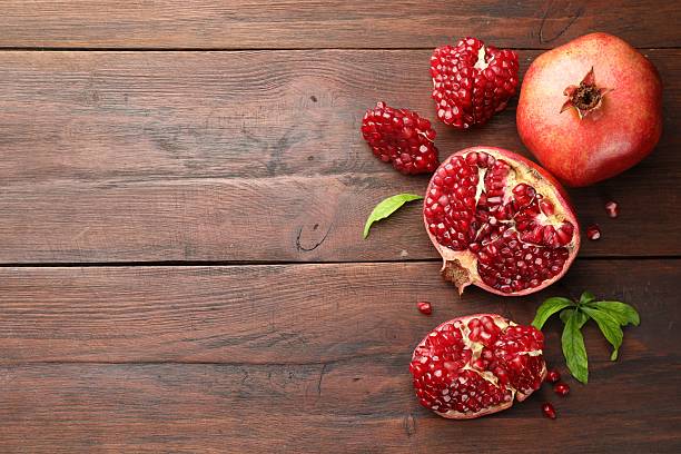 istock Fresh pomegranates and green leaves on wooden table, flat lay. Space for text 2244715211