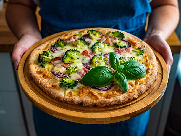 istock Woman holding circle pizza broccoli with bacon and mozzarella cheese on cutting board 2244715471